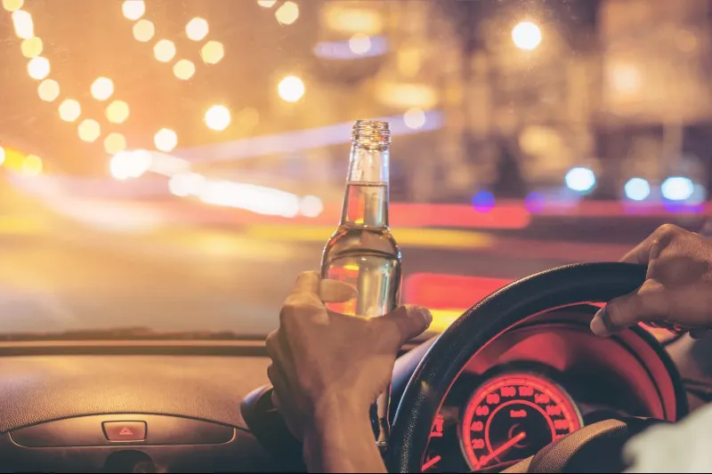 a person holding an alcohol bottle while driving