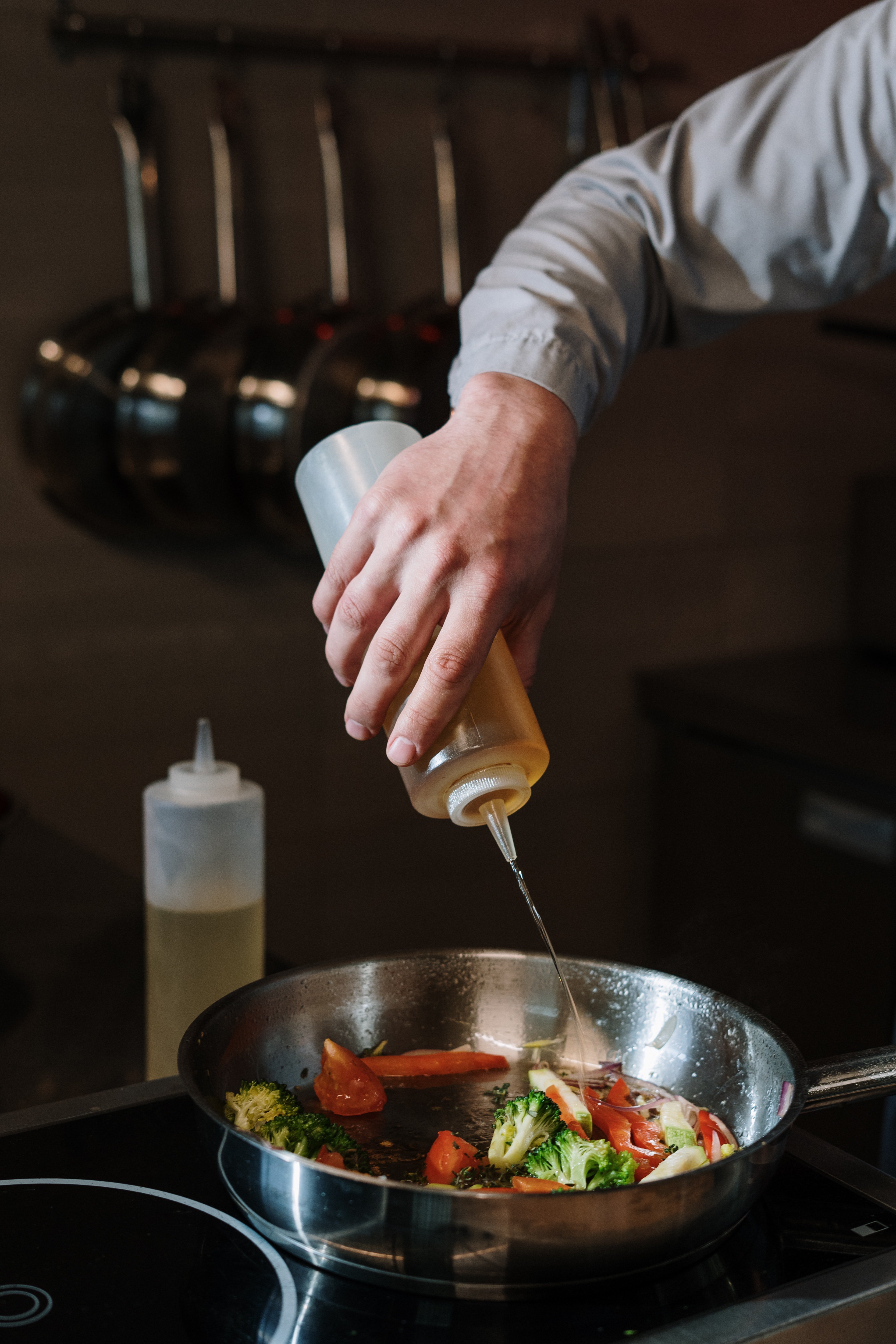 A man putting oil in a pan with vegetables
