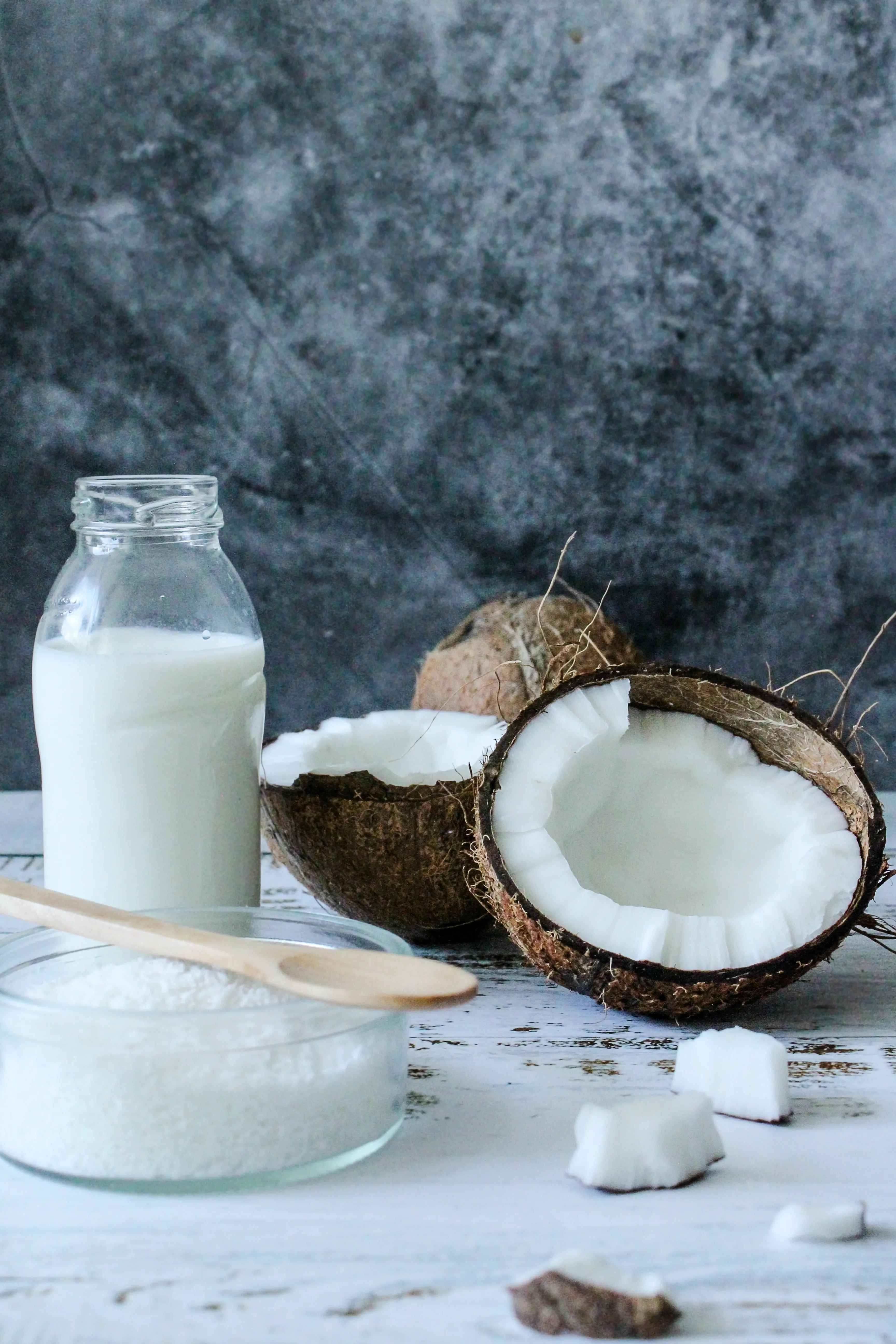 Coconut milk kept on a table in a bottle with some coconut pieces and grated coconut