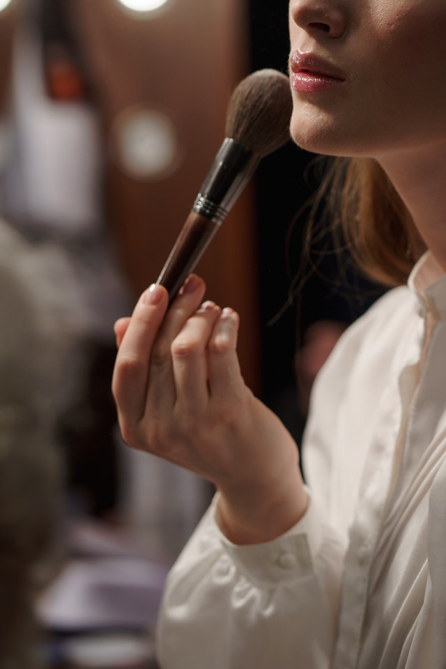 A woman using a powder brush on her face