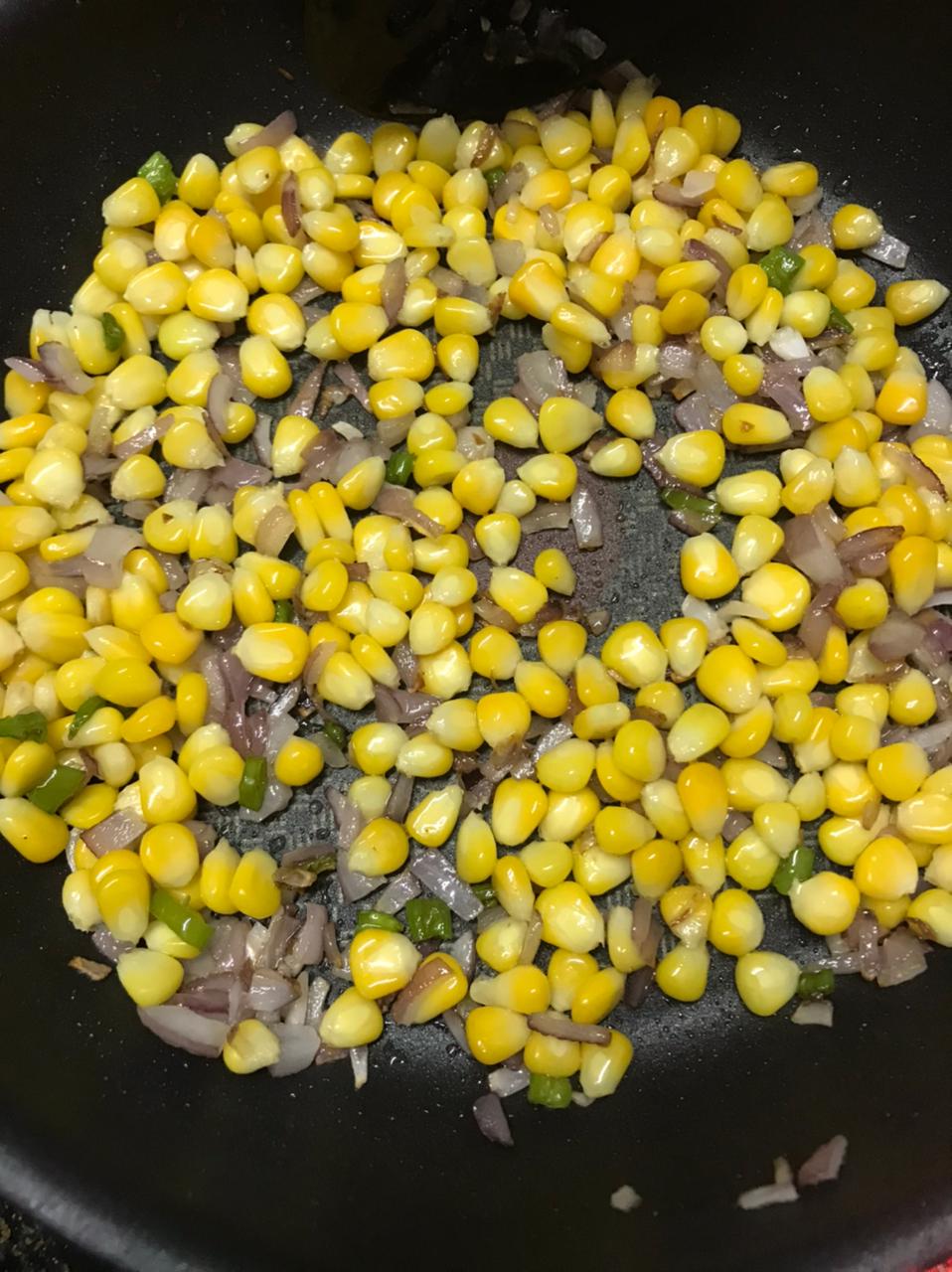 boiled corn added to the onions and green chillies mix in the pan
