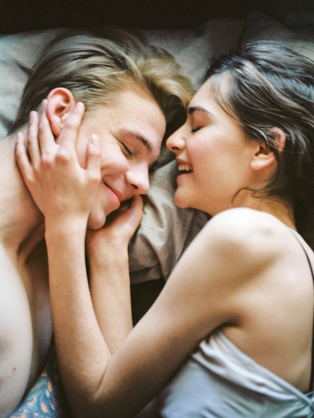 A man and woman laying on bed smiling at each other