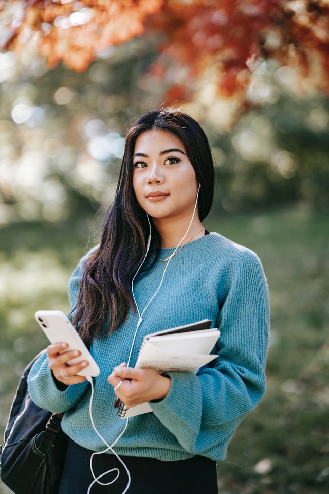 A women wearing headphones holding a phone and a notebook