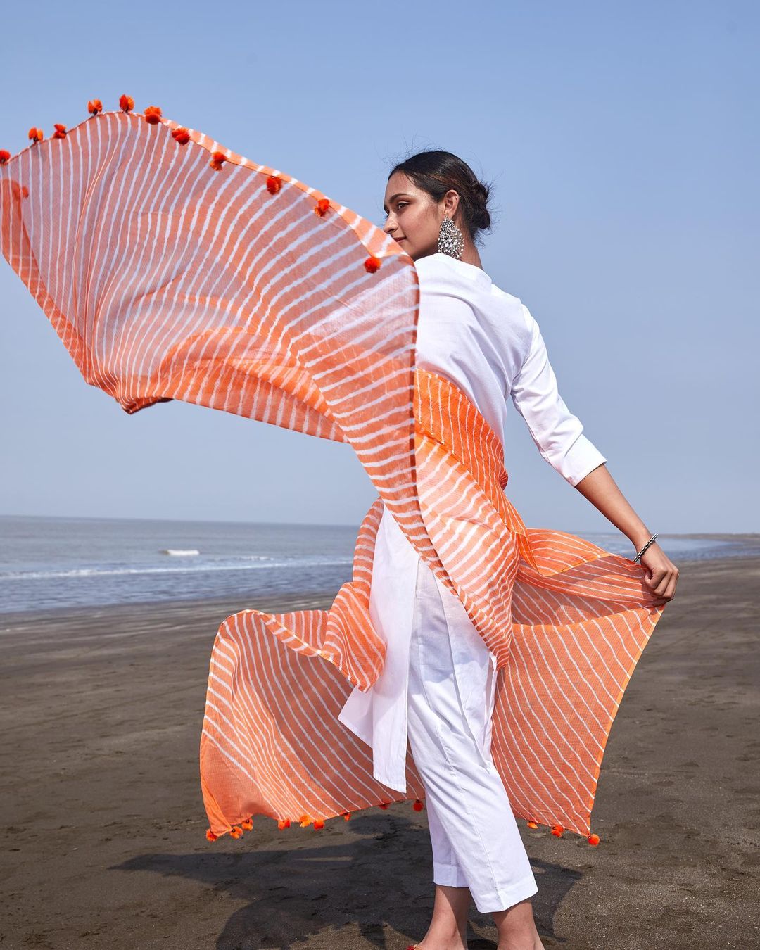 A lady wearing white suit with orange dupatta by the beach