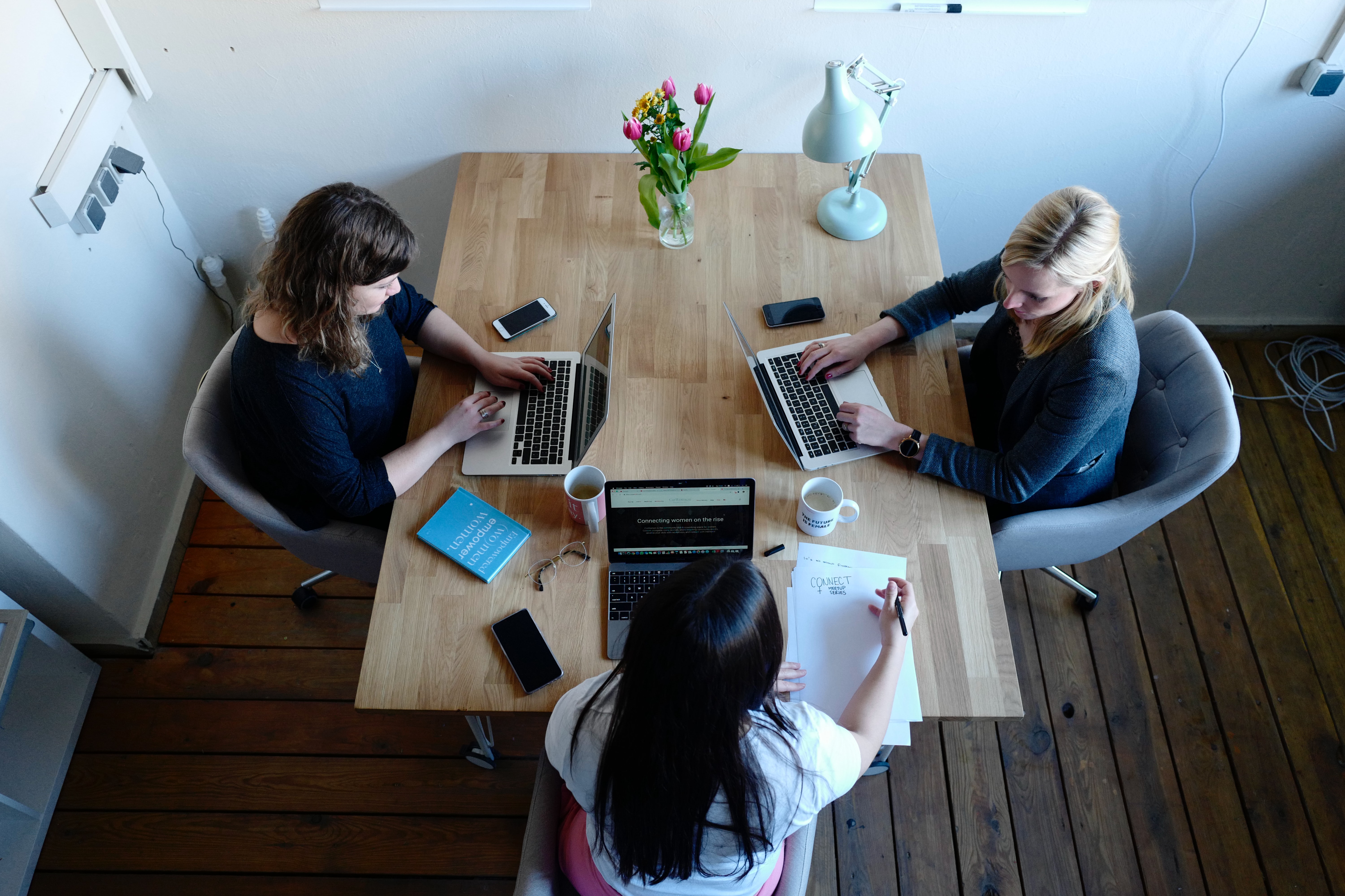 3 women sitting around a table and using laptop