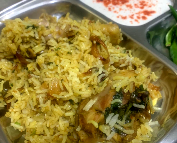 A plate with chicken biryani, curd and green chillies