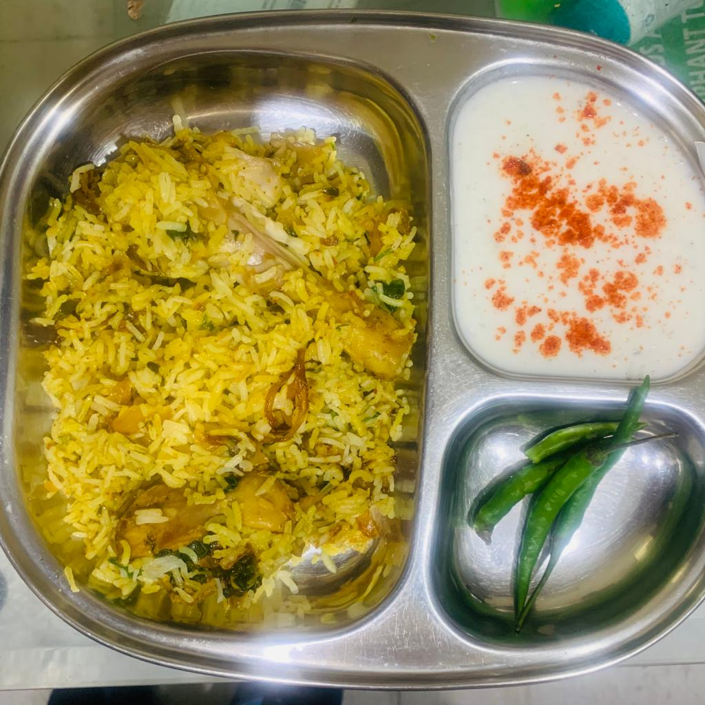 a plate with biryani, curd and green chillies