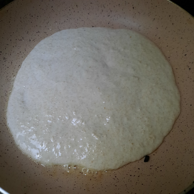 batter of pizza base spread and cooking in a pan
