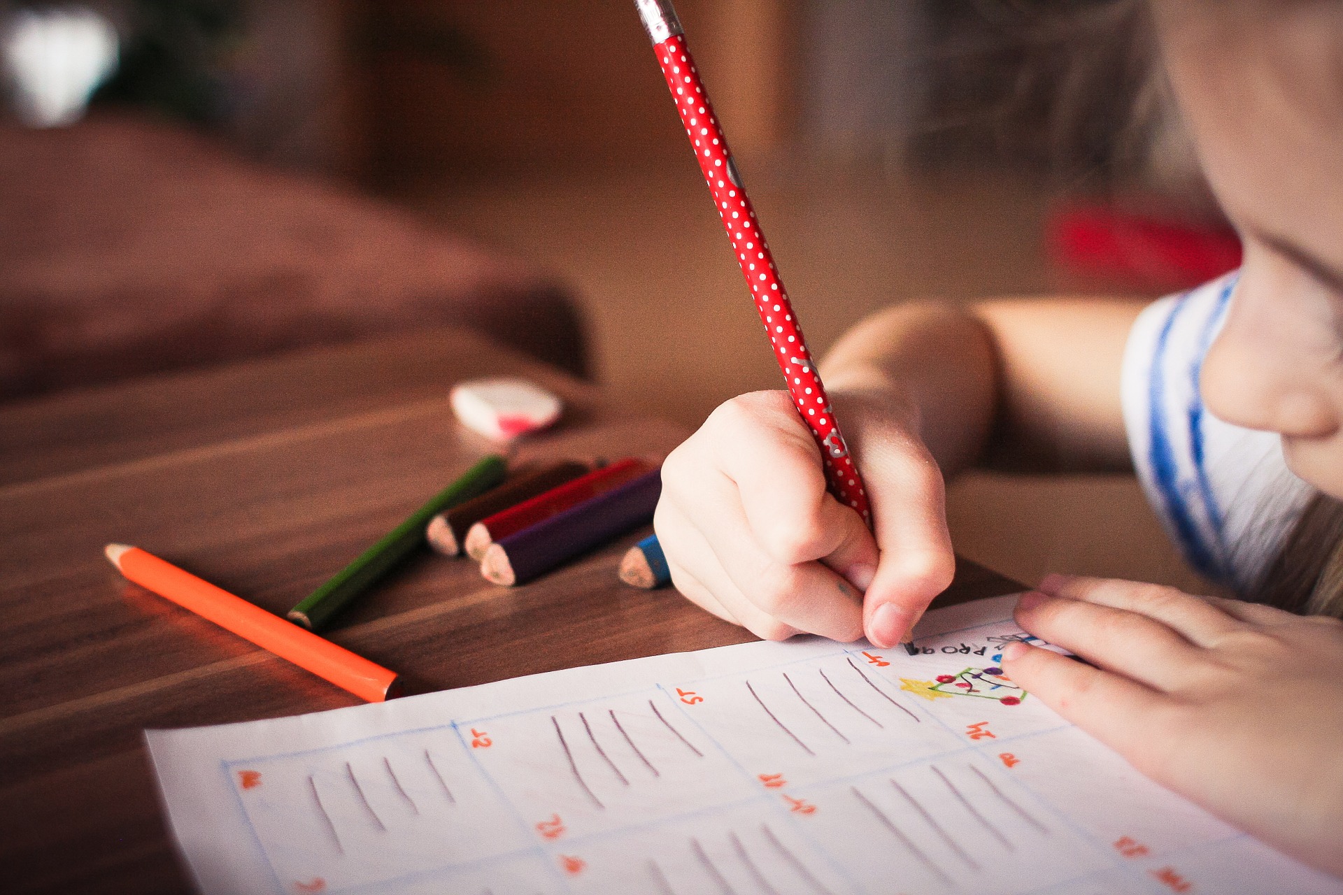 a child writing in a book with colored pencils strewn across the table